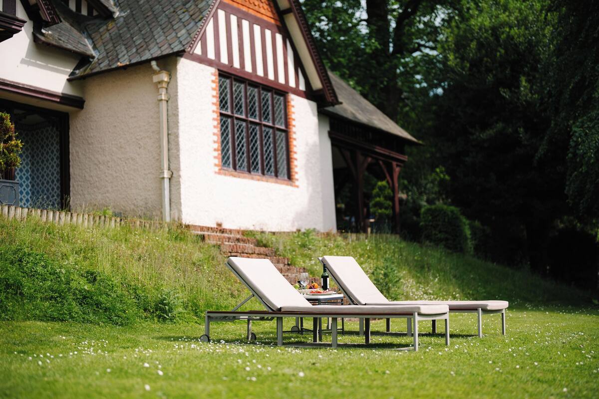 A house with a white exterior and brown trim, a window with a grid pattern, and a small table with a glass of water and a plate of food.