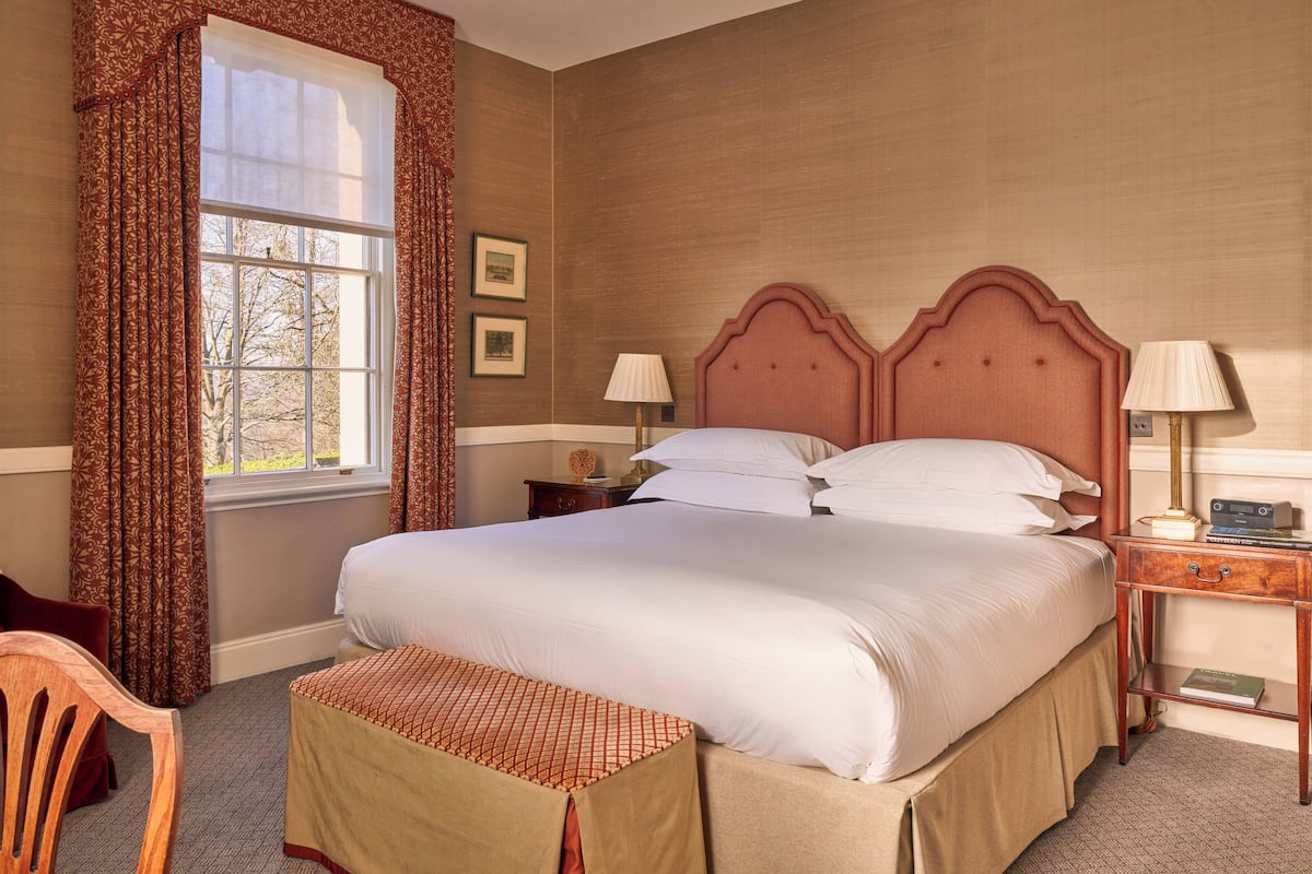 A neatly made bed with a wooden headboard, a bedside table with a lamp, and a window with curtains.