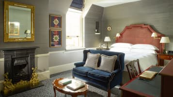 A hotel room with a fireplace, a blue sofa, a bed with a red headboard, and a nightstand with lamps.