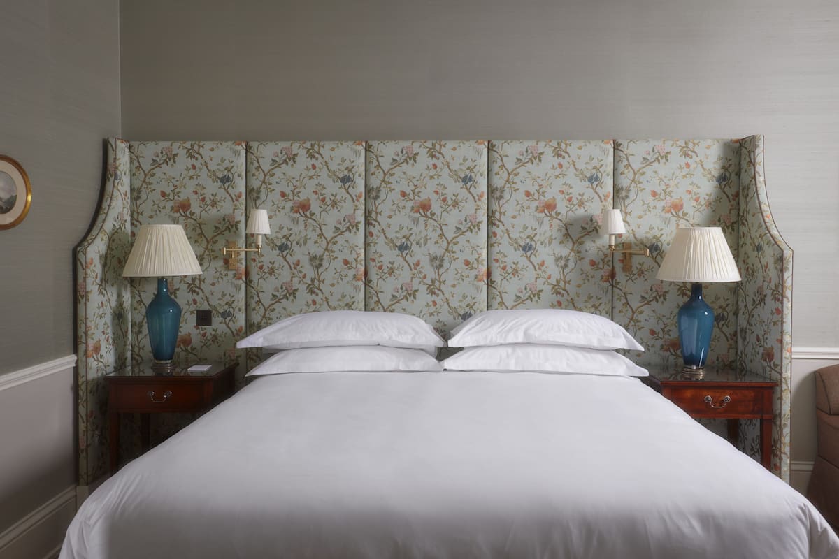 A neatly made bed with white linens, two bedside tables with lamps, and floral wallpaper.