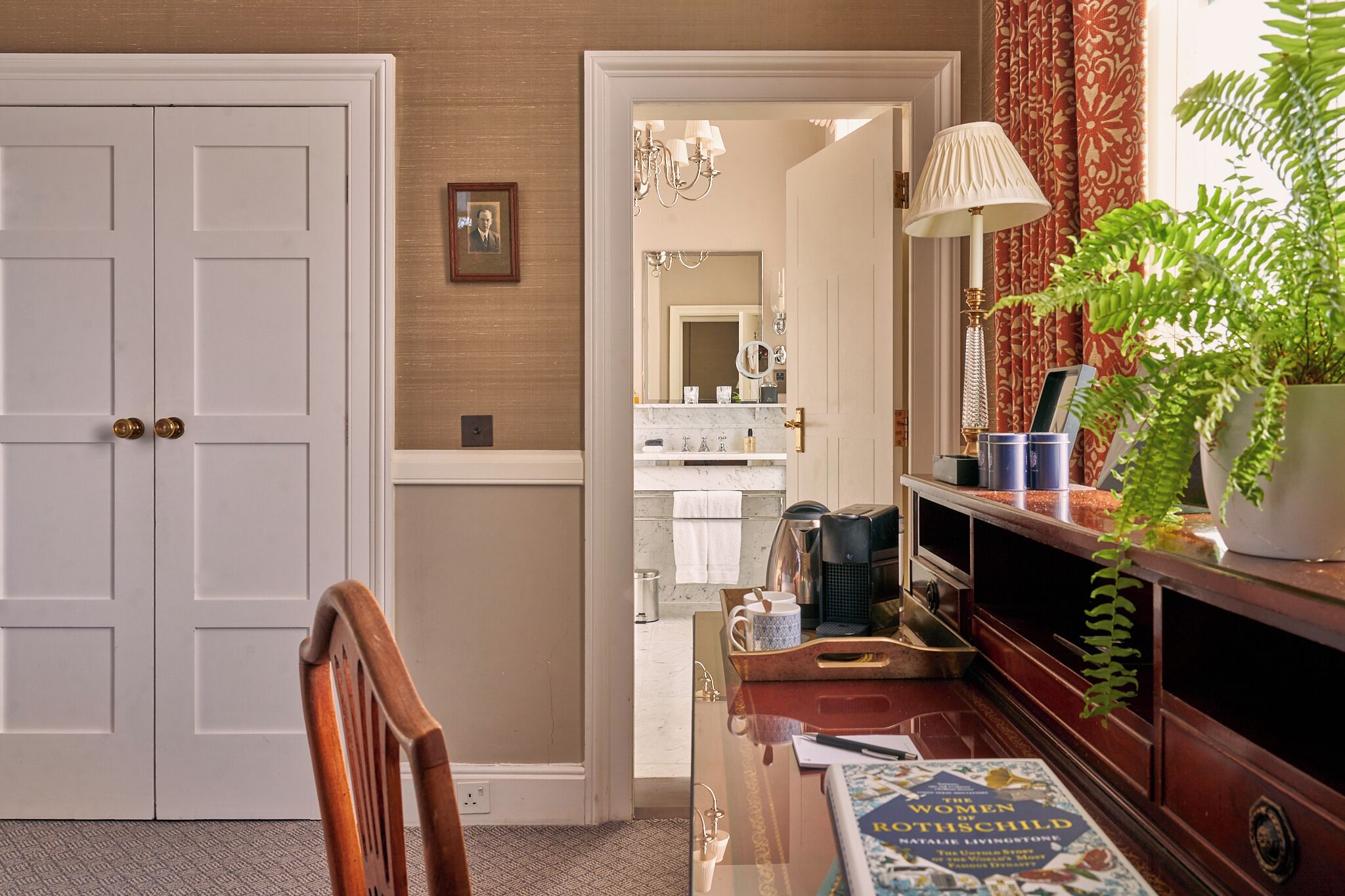 A hallway with a wooden chair, a desk with a book, and a potted plant.