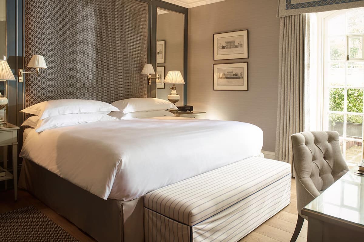 A hotel room with a large bed, bedside lamps, a chair, a table, and framed pictures on the wall.