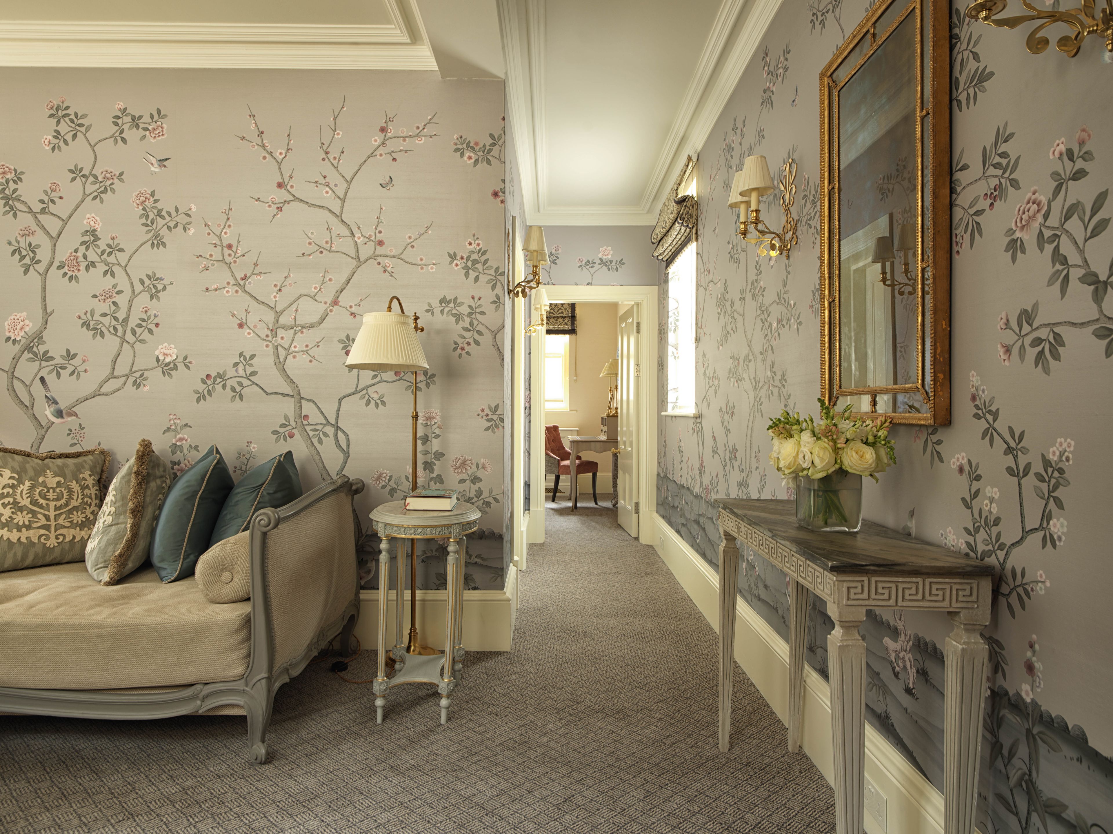A room with a sofa, a small table with a lamp, a console table with a vase, and a mirror.