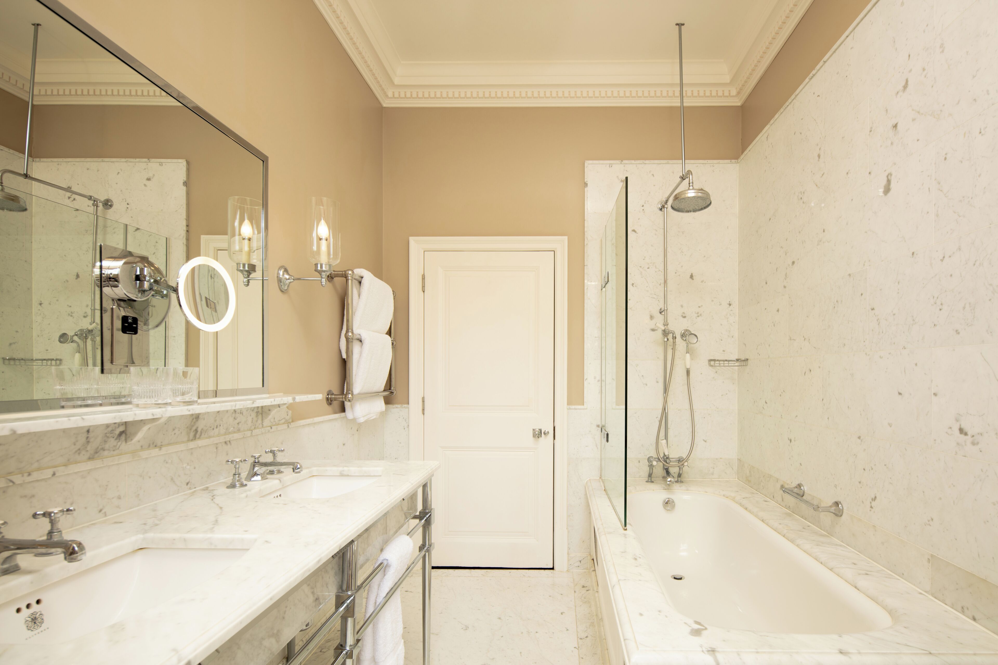 A bathroom with two sinks, a mirror, a towel rack, a shower, and a door.