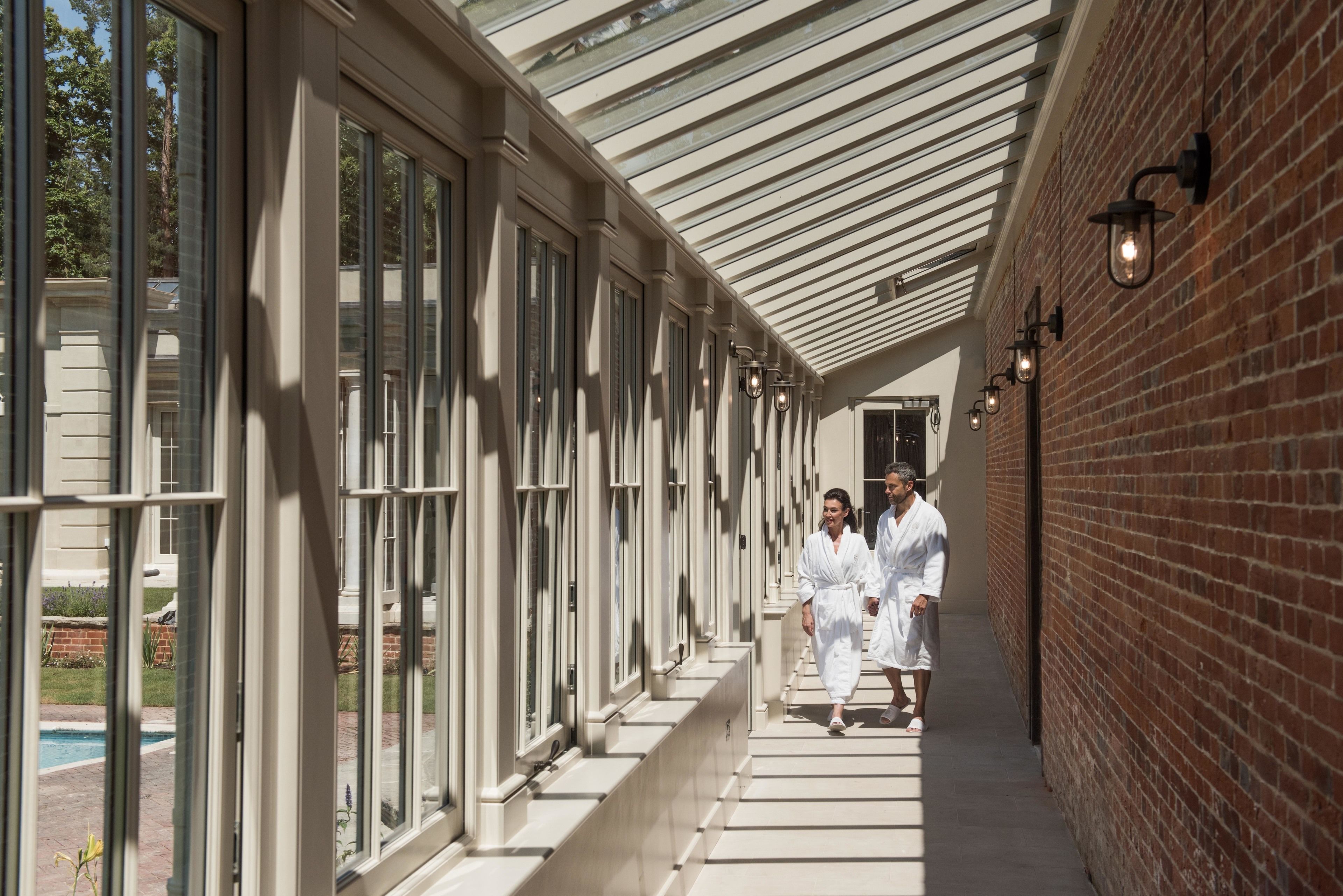 A covered corridor with large windows and brick walls, leading to a pool area.