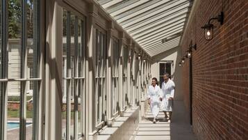 A covered corridor with large windows and brick walls, leading to a pool area.