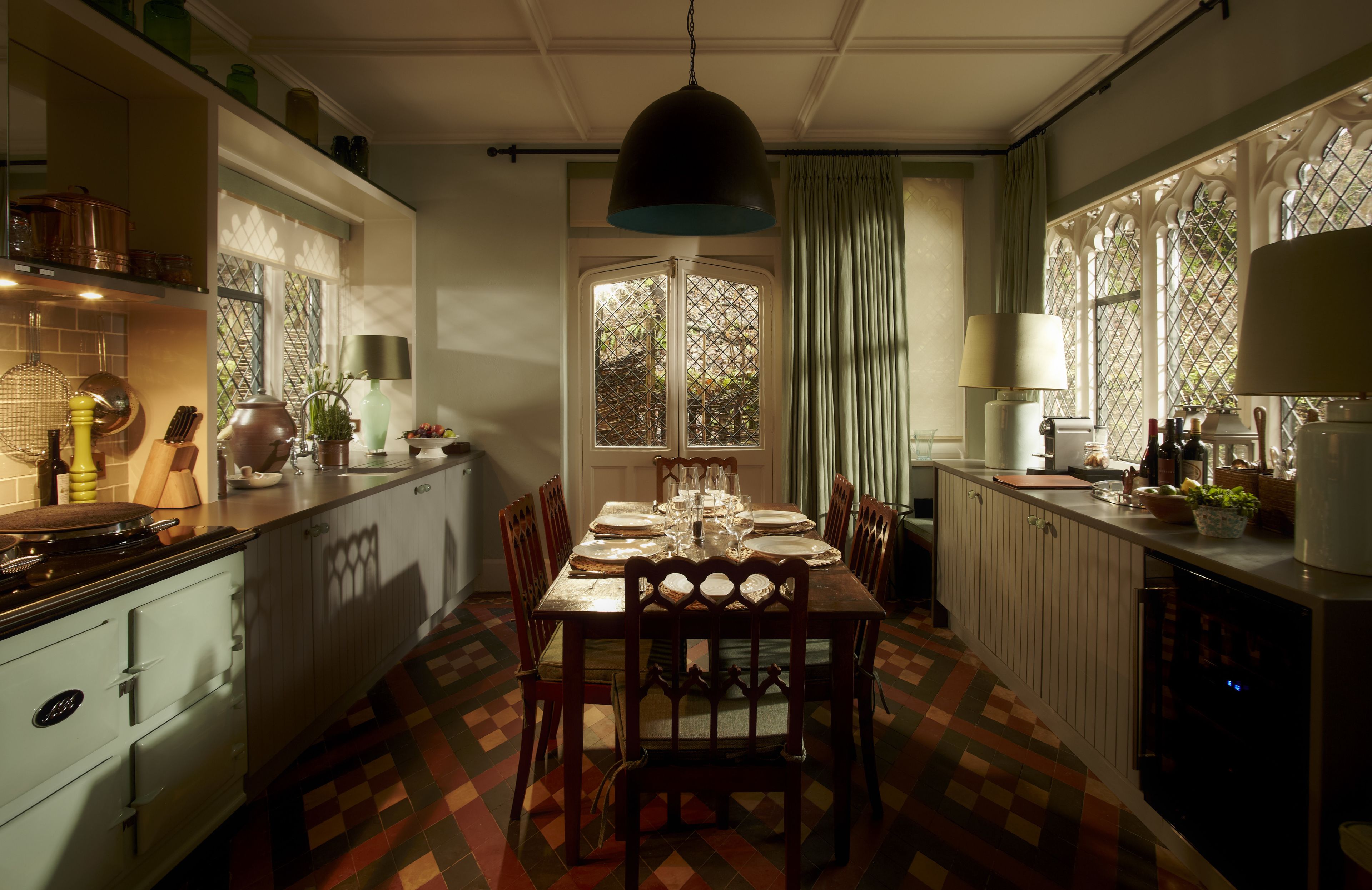 A traditional dining room with a large table set for six, surrounded by wooden chairs. A window with a lattice design allows natural light to enter.