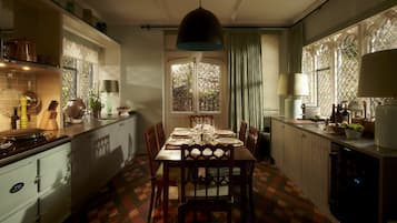 A traditional dining room with a large table set for six, surrounded by wooden chairs. A window with a lattice design allows natural light to enter.