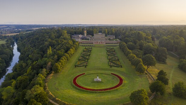 An aerial view of a large estate with a central lawn, a circular garden, and a building with a tower.