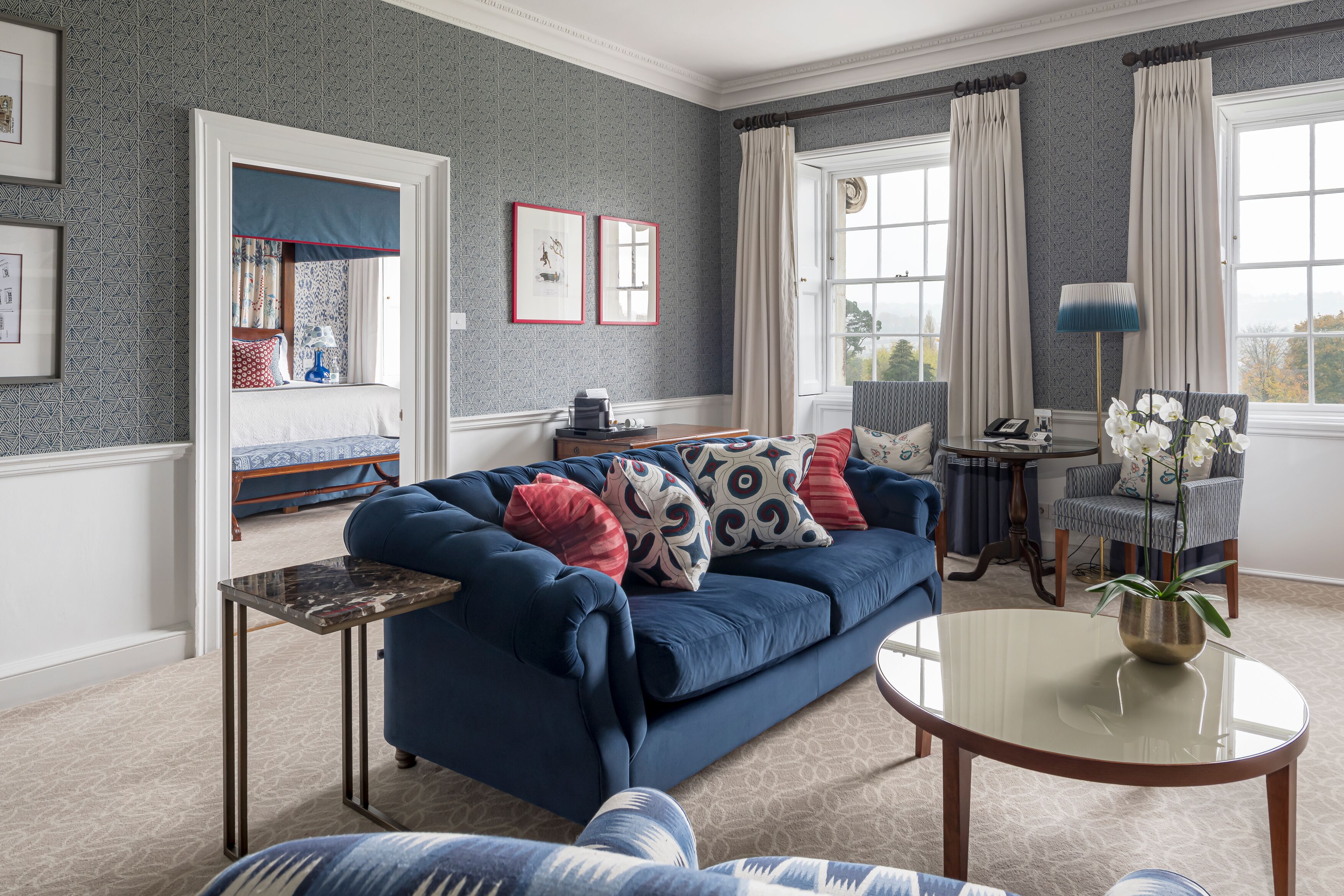 A living room with a blue sofa, a glass coffee table, and a view of the outdoors through large windows.