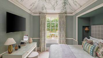 A bedroom with a bed, a dresser, a mirror, a flat-screen TV, and a window with curtains.