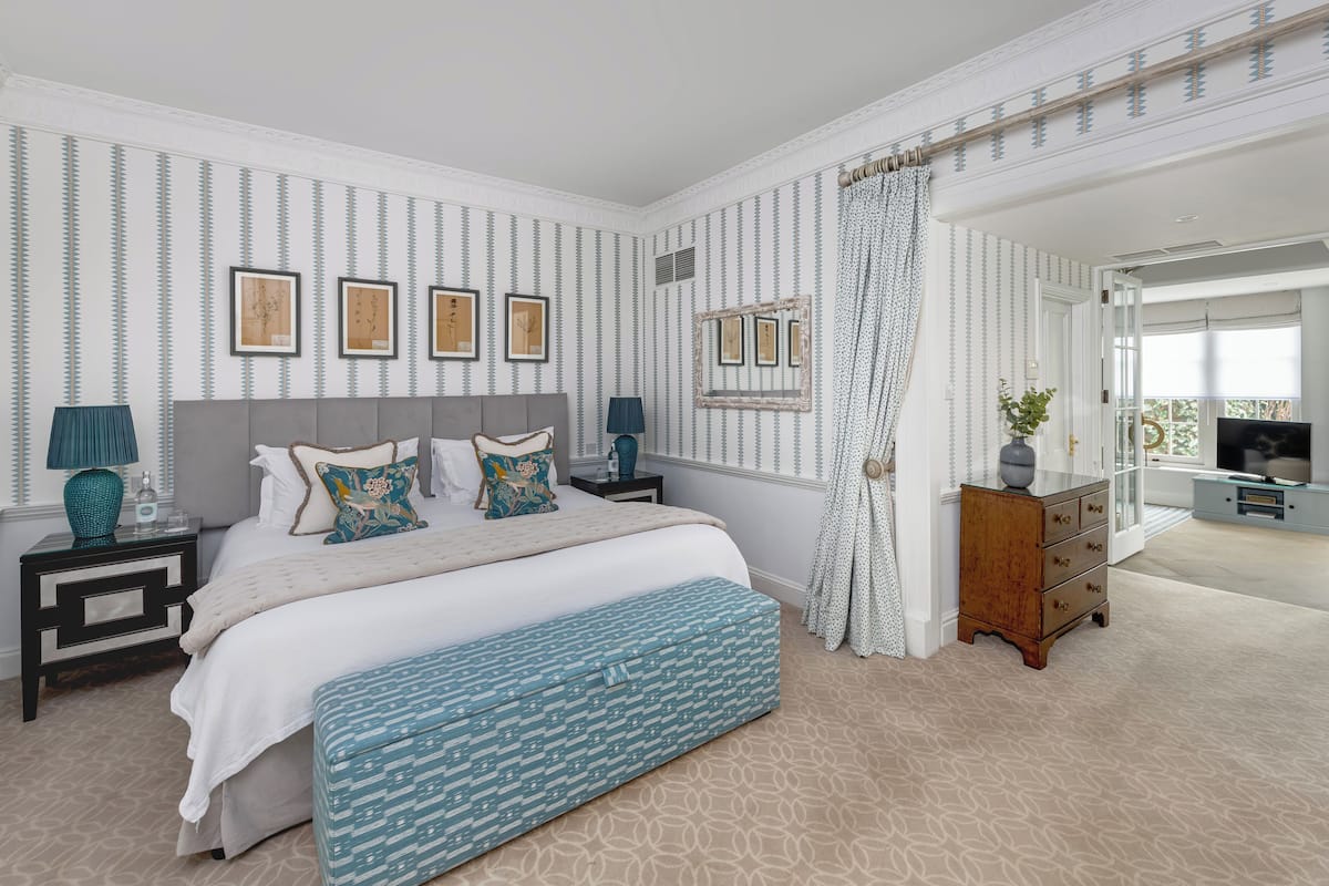 Quarto com cama, mesas de cabeceira, cômoda, um banco e vista para o exterior.