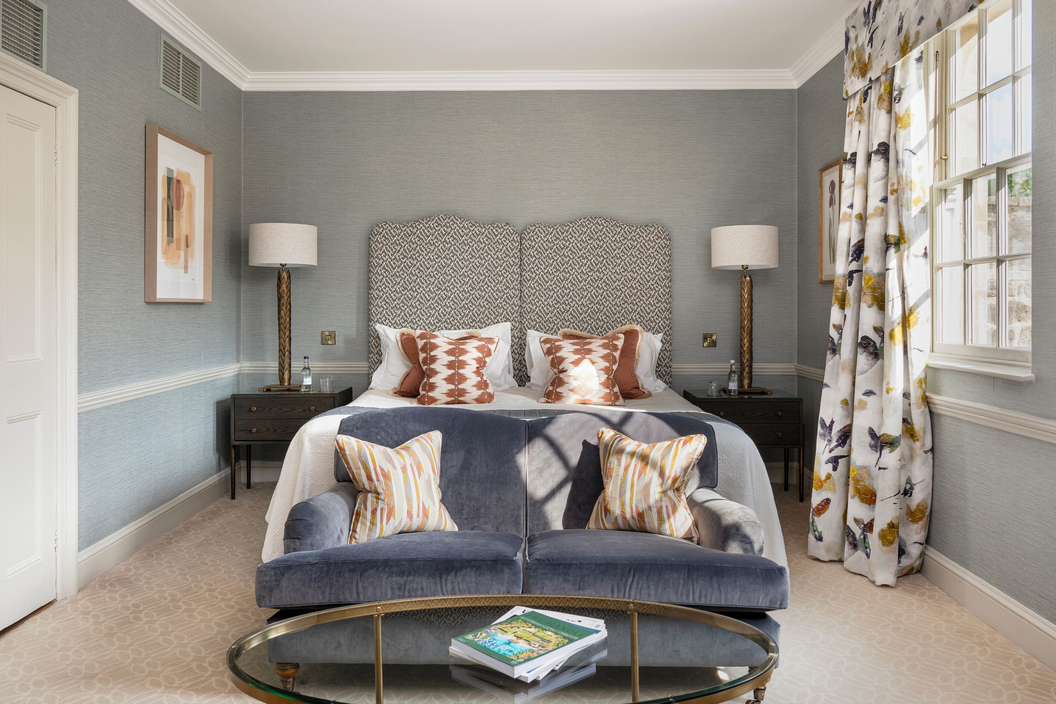 A bedroom with a bed, two bedside tables, a sofa, a coffee table, and a window with curtains.