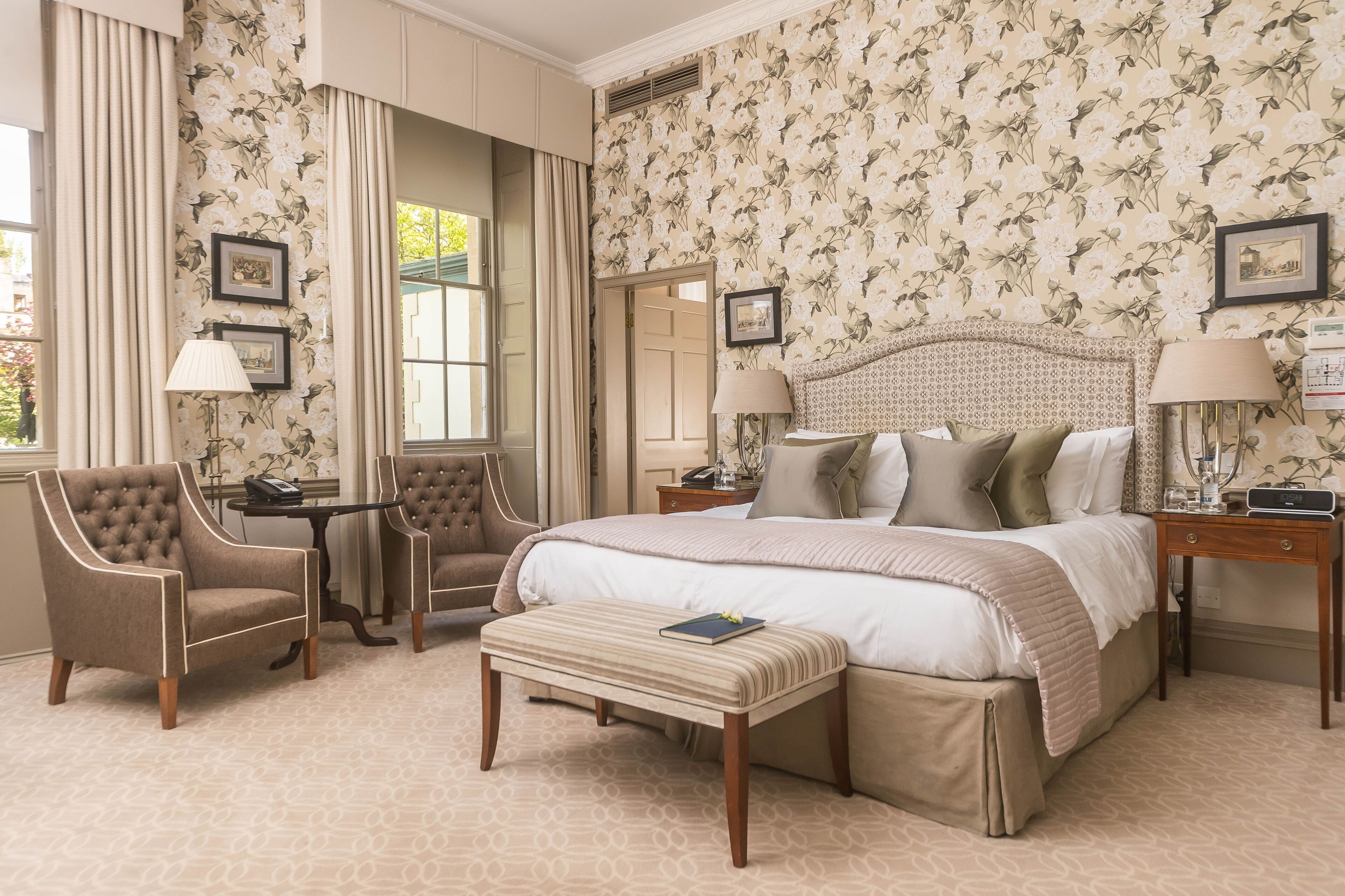 A spacious bedroom with a large bed, two armchairs, a small table, and a bench.