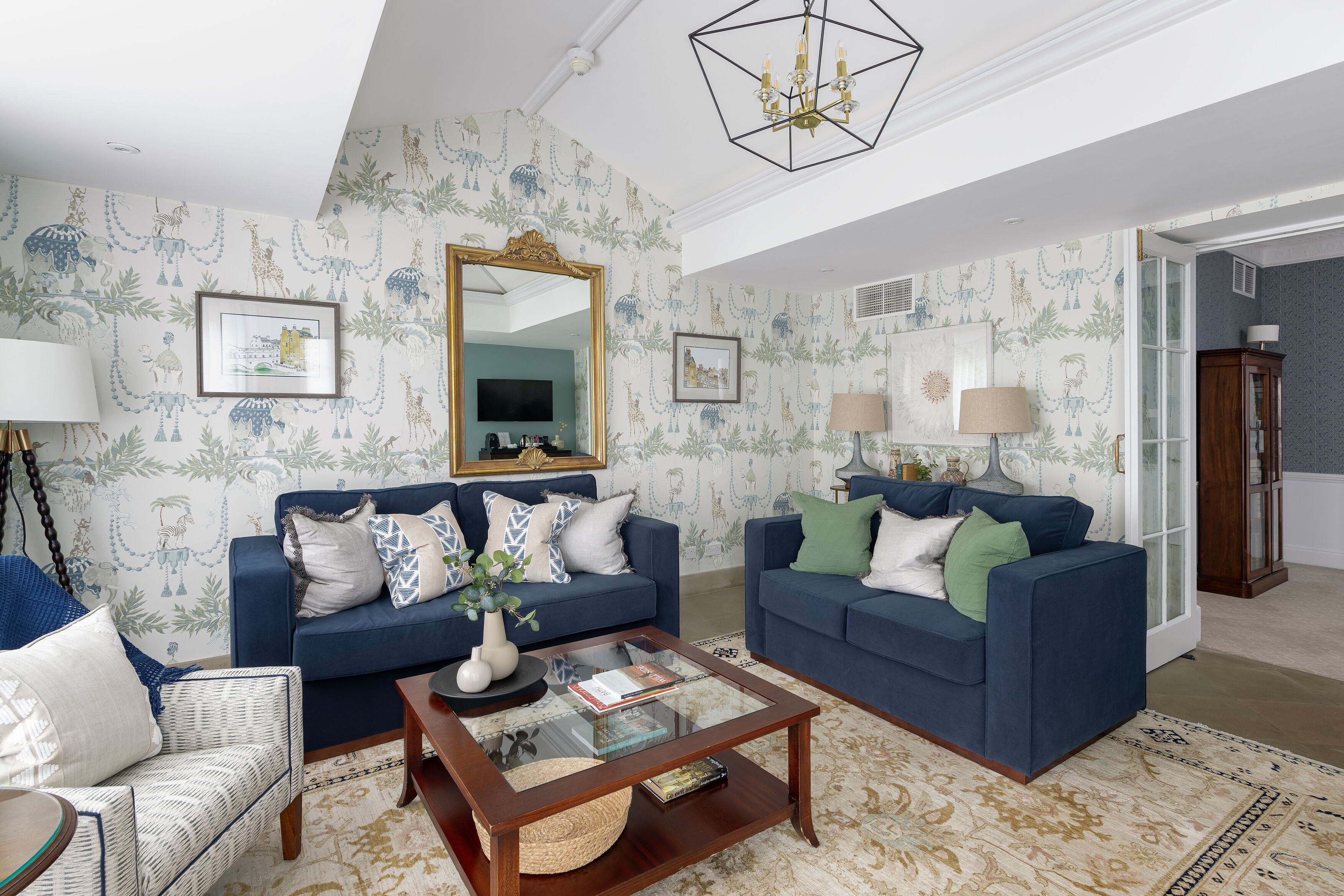 A living room with two blue sofas, a glass coffee table, and patterned wallpaper.