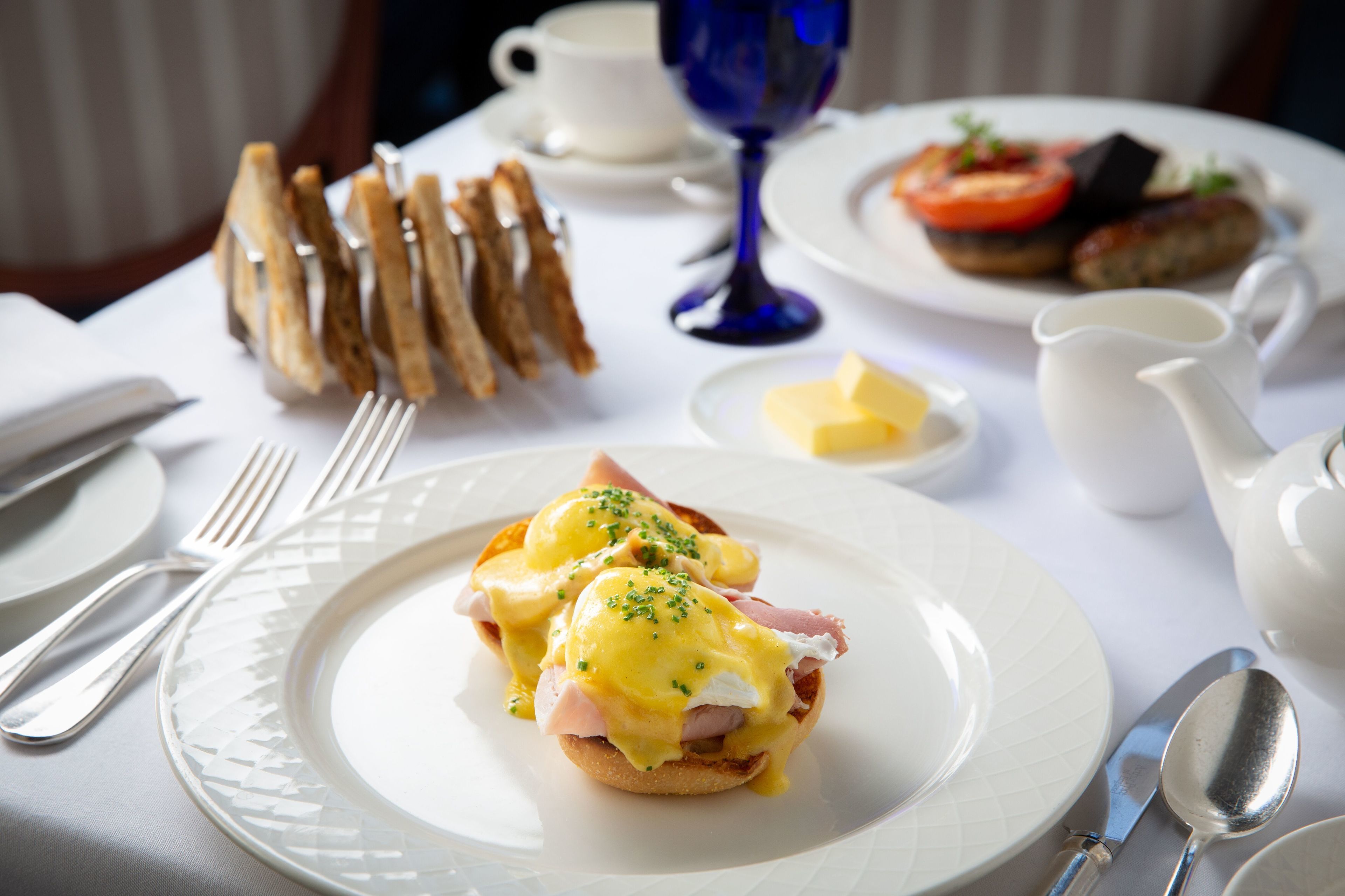 A breakfast setting with a plate of eggs benedict, toast, and a cup of coffee.