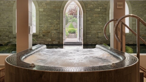 A hot tub with a stone wall backdrop and a view of a garden through an arched doorway. - The Royal Crescent Hotel & Spa (Bath)