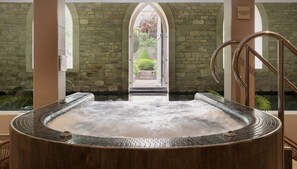 A hot tub with a stone wall backdrop and a view of a garden through an arched doorway. - The Royal Crescent Hotel & Spa (Bath)