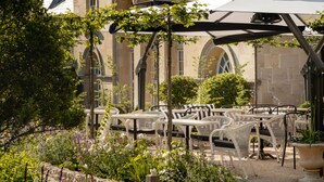 An outdoor seating area with white wicker furniture, a pergola with a white umbrella, and a stone building with arches in the background. - The Royal Crescent Hotel & Spa (Bath)