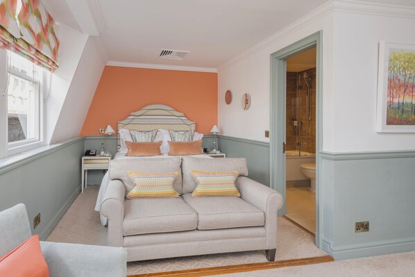 A bedroom with a bed, a sofa, a nightstand, and a bathroom visible through an open door.