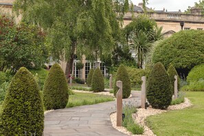 Un jardín ajardinado con un sendero de piedra, setos recortados y un edificio al fondo.