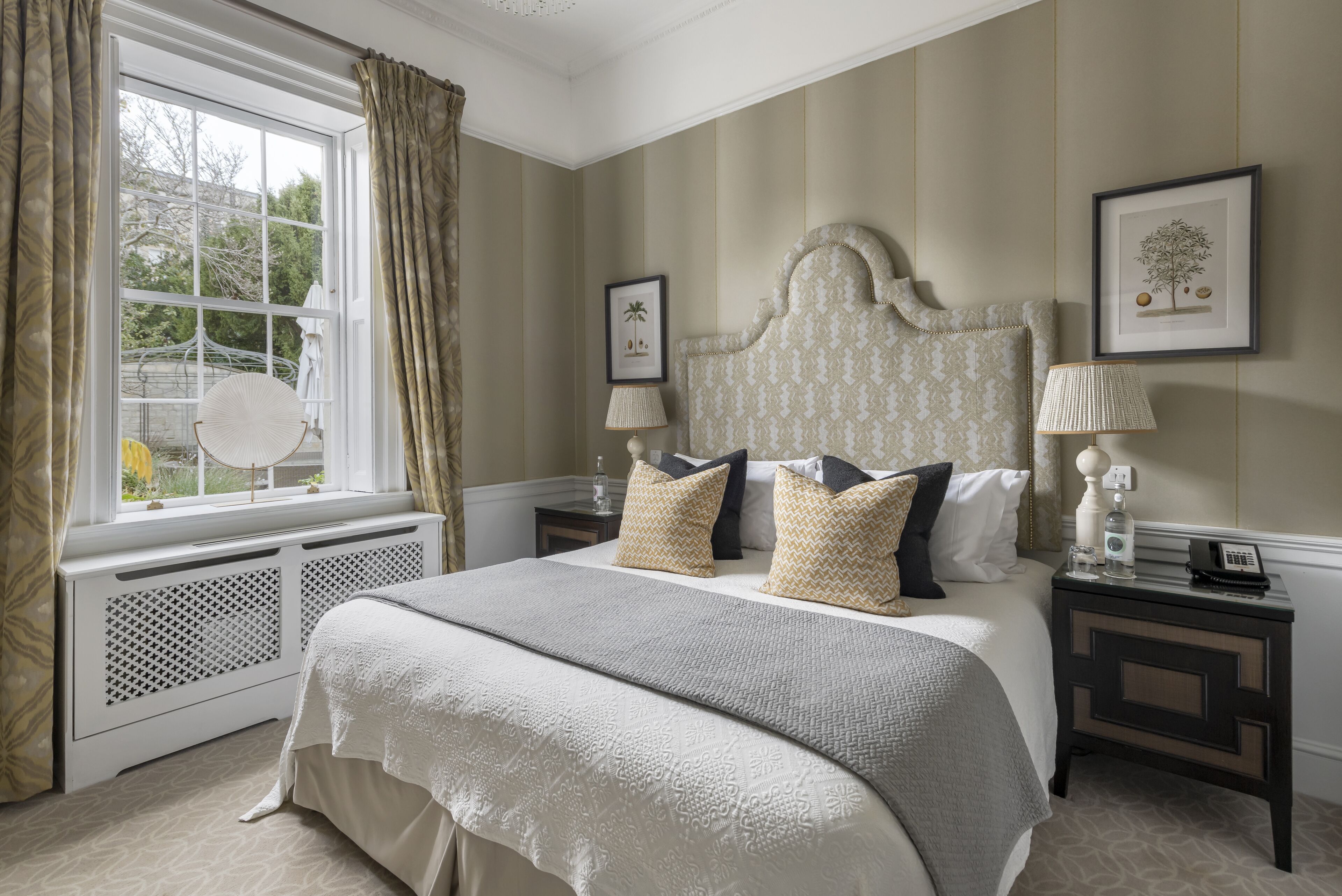 A bedroom with a large bed, a window with curtains, a bedside table with a lamp, and a framed picture on the wall.
