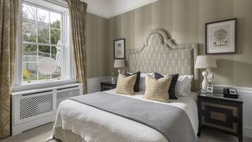 A bedroom with a large bed, a window with curtains, a bedside table with a lamp, and a framed picture on the wall.