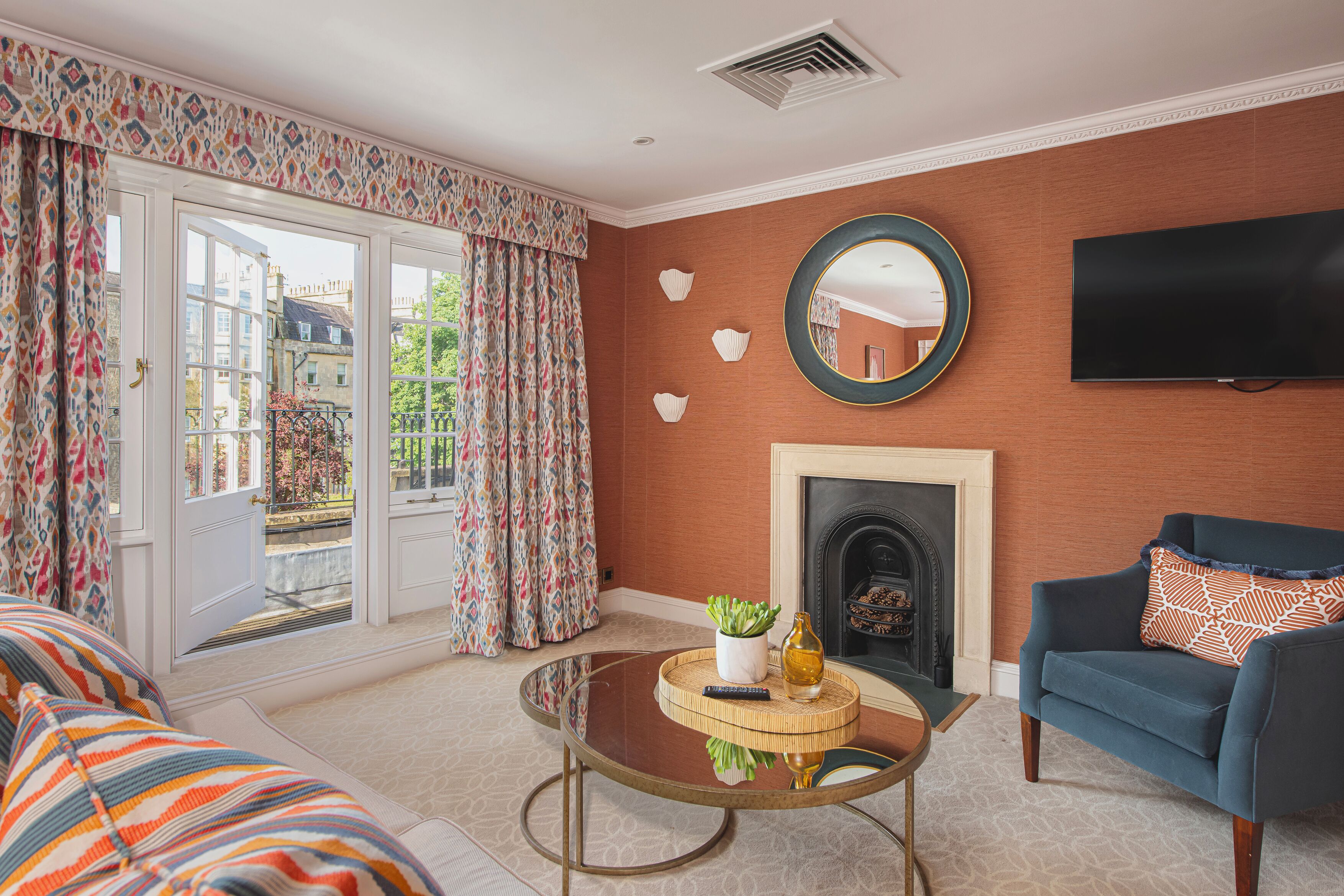 A living room with a sofa, a round glass coffee table, a blue armchair, a fireplace, and a TV mounted on the wall.