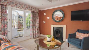 A living room with a sofa, a round glass coffee table, a blue armchair, a fireplace, and a TV mounted on the wall.