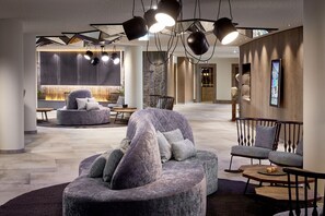 A modern lounge area with a curved seating arrangement, pendant lighting, and a digital display on the wall.