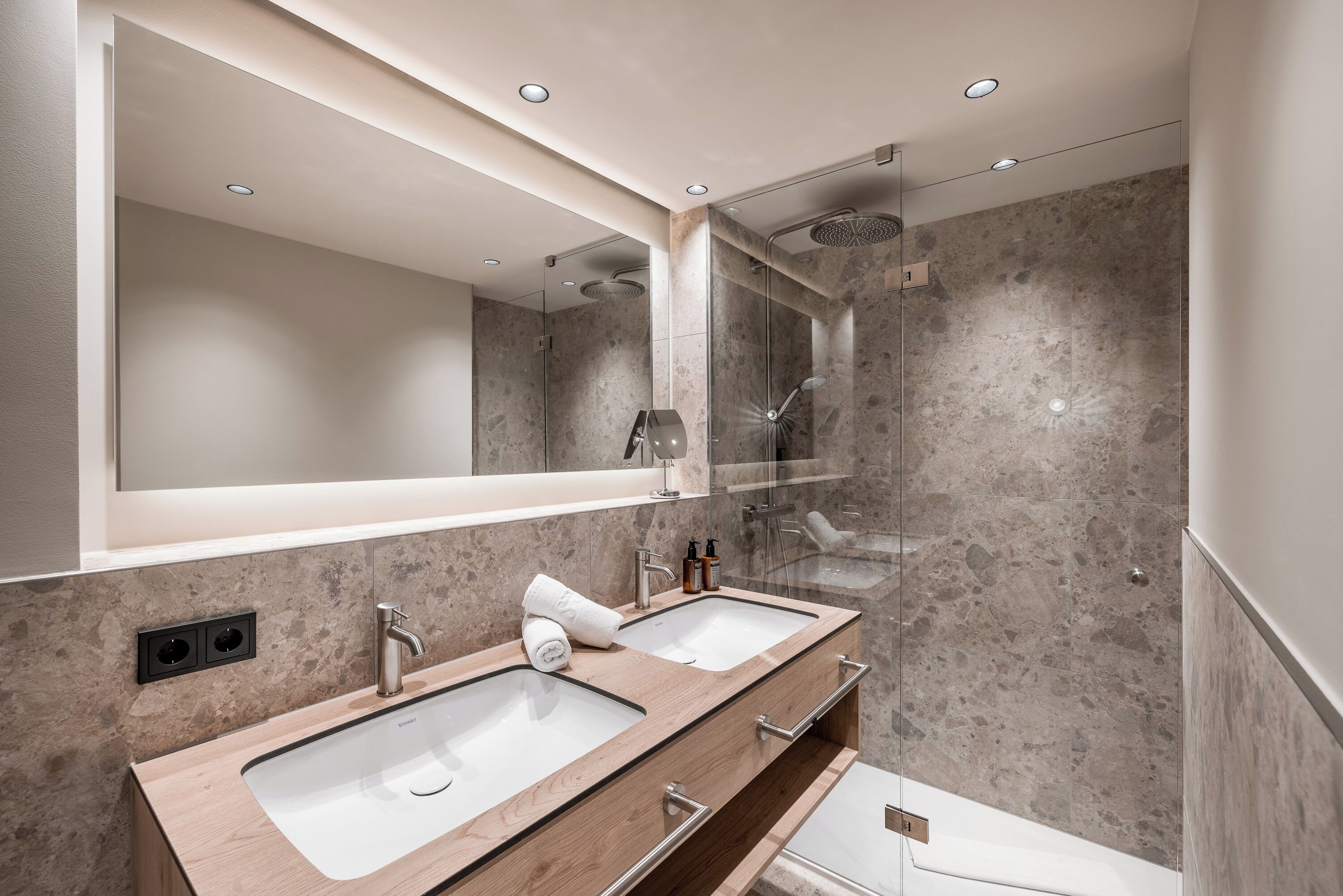 Un baño moderno con dos lavamanos, un espejo grande y una ducha.