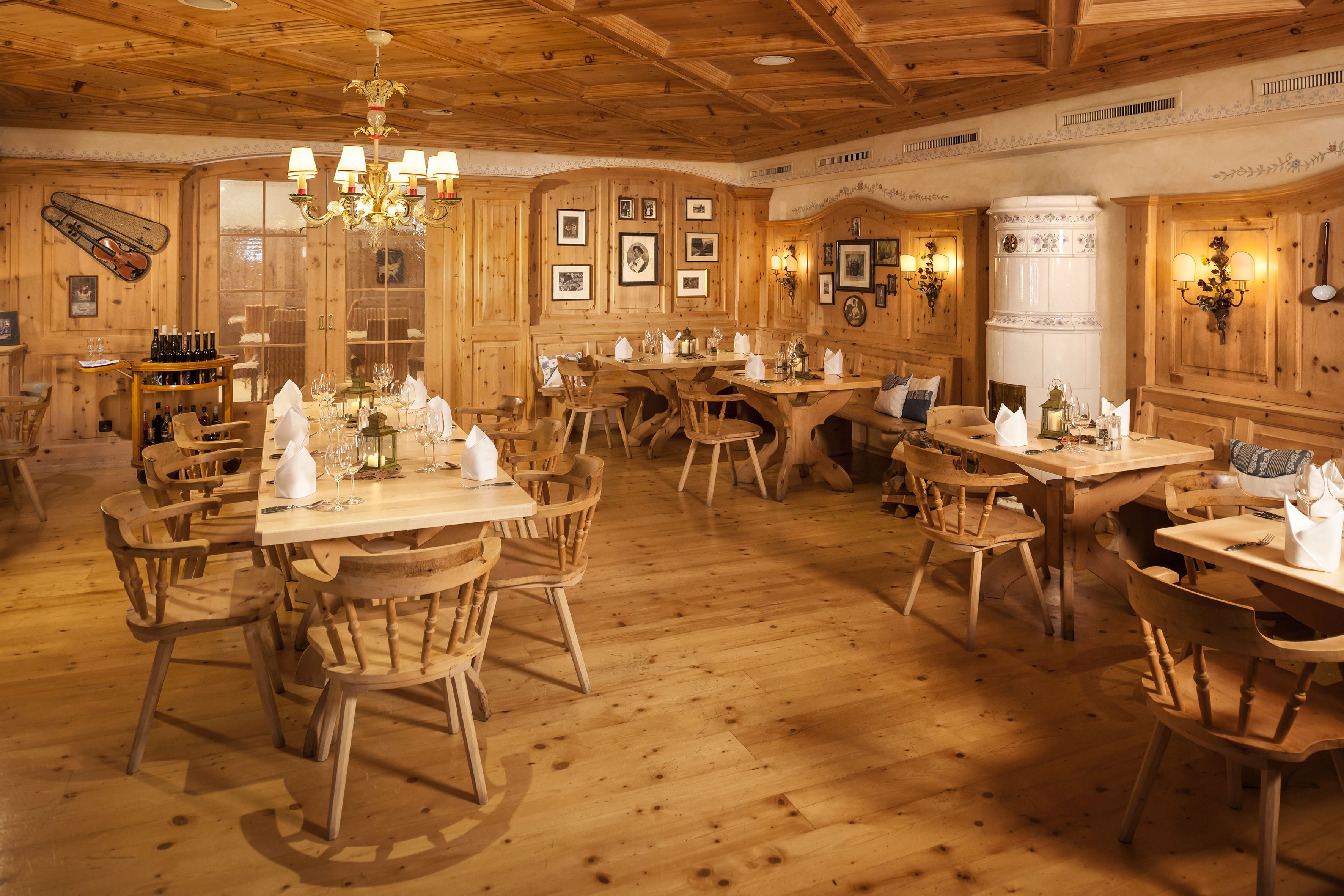 A wooden interior with multiple dining tables and chairs, a chandelier, and framed pictures on the walls.