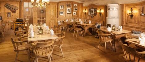 A wooden interior with multiple dining tables and chairs, a chandelier, and framed pictures on the walls.