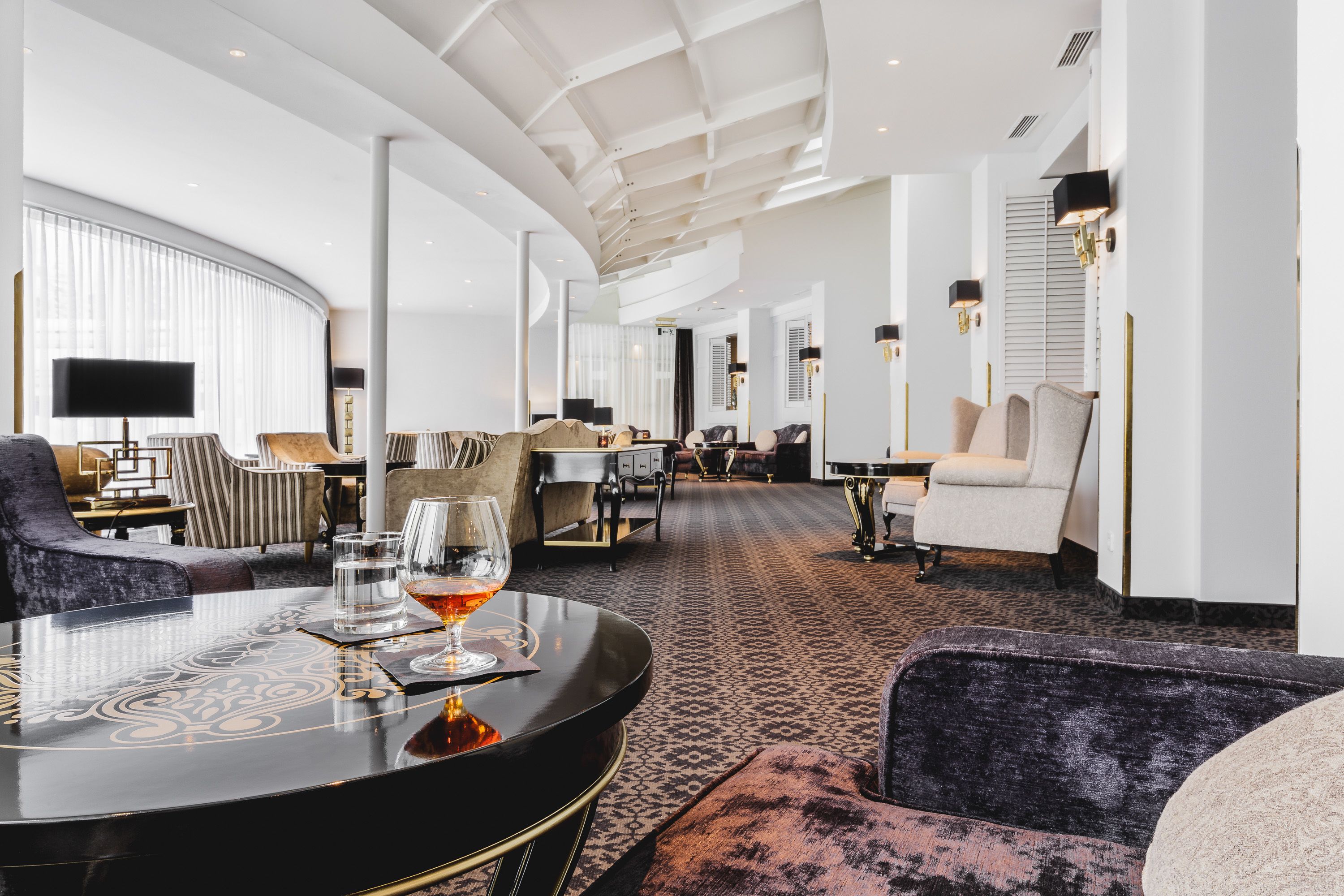 Eine moderne Hotelhalle mit gewölbter Decke, komfortablen Sitzgelegenheiten und einem runden Tisch mit Gläsern.