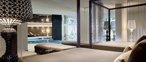 A modern hotel room with a large bed, a sitting area with a pool view, and a decorative lamp.