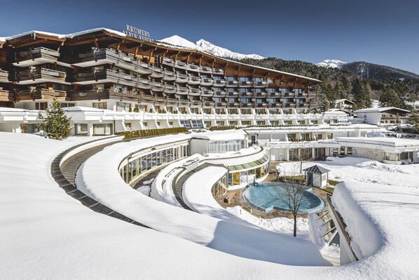 Ein mehrstöckiges Hotel mit Skigebietsname, Poolbereich und verschneiter Umgebung.