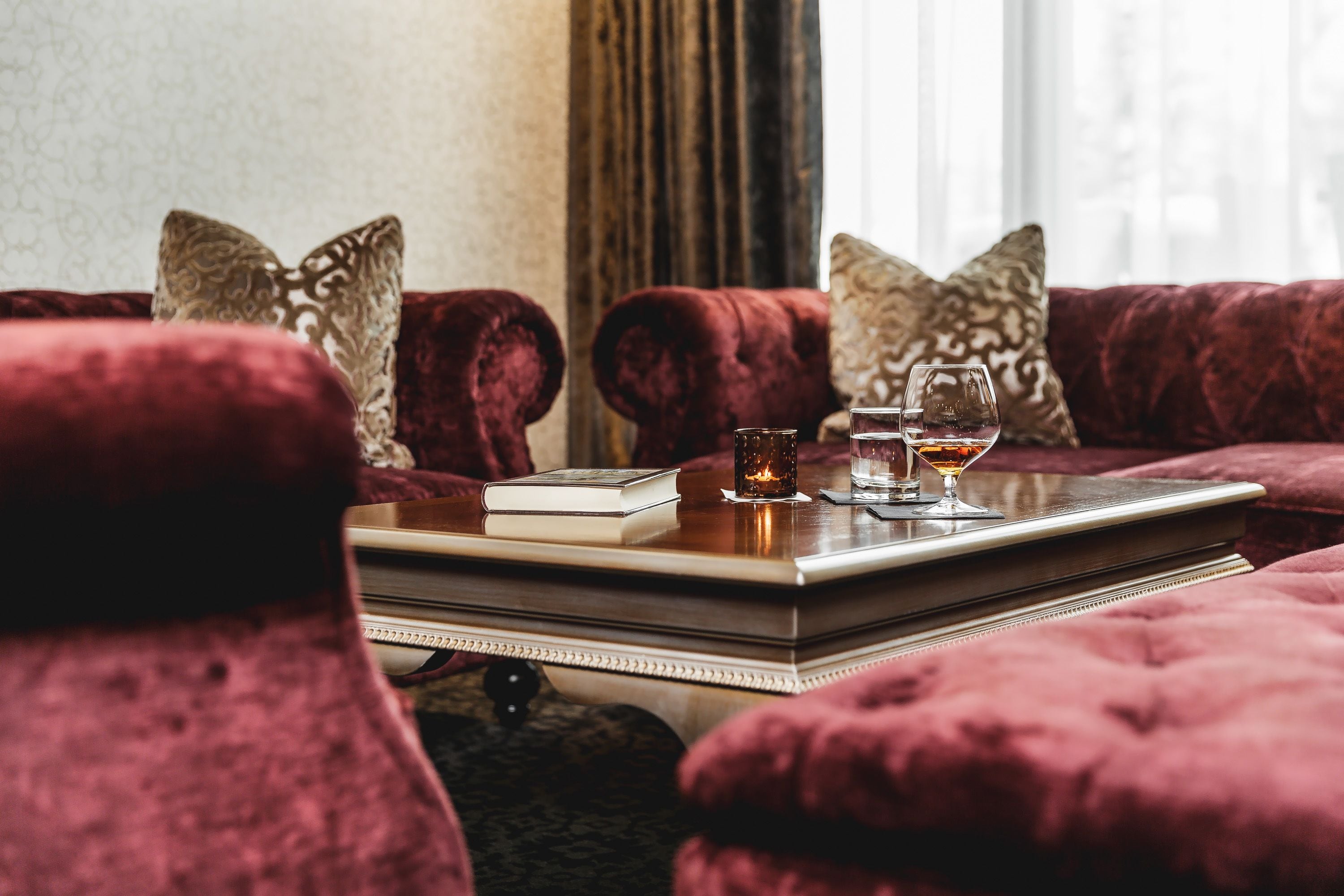 A plush red sofa with a tray table, a book, and two glasses of wine.
