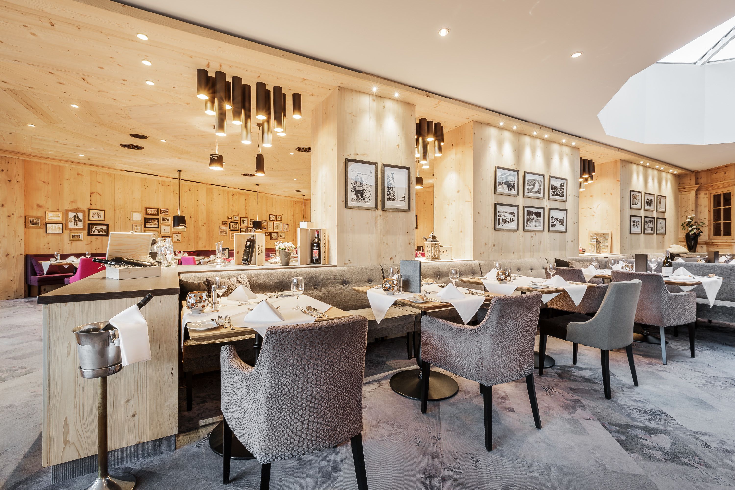 A restaurant with wooden walls, multiple dining tables, and modern lighting fixtures.