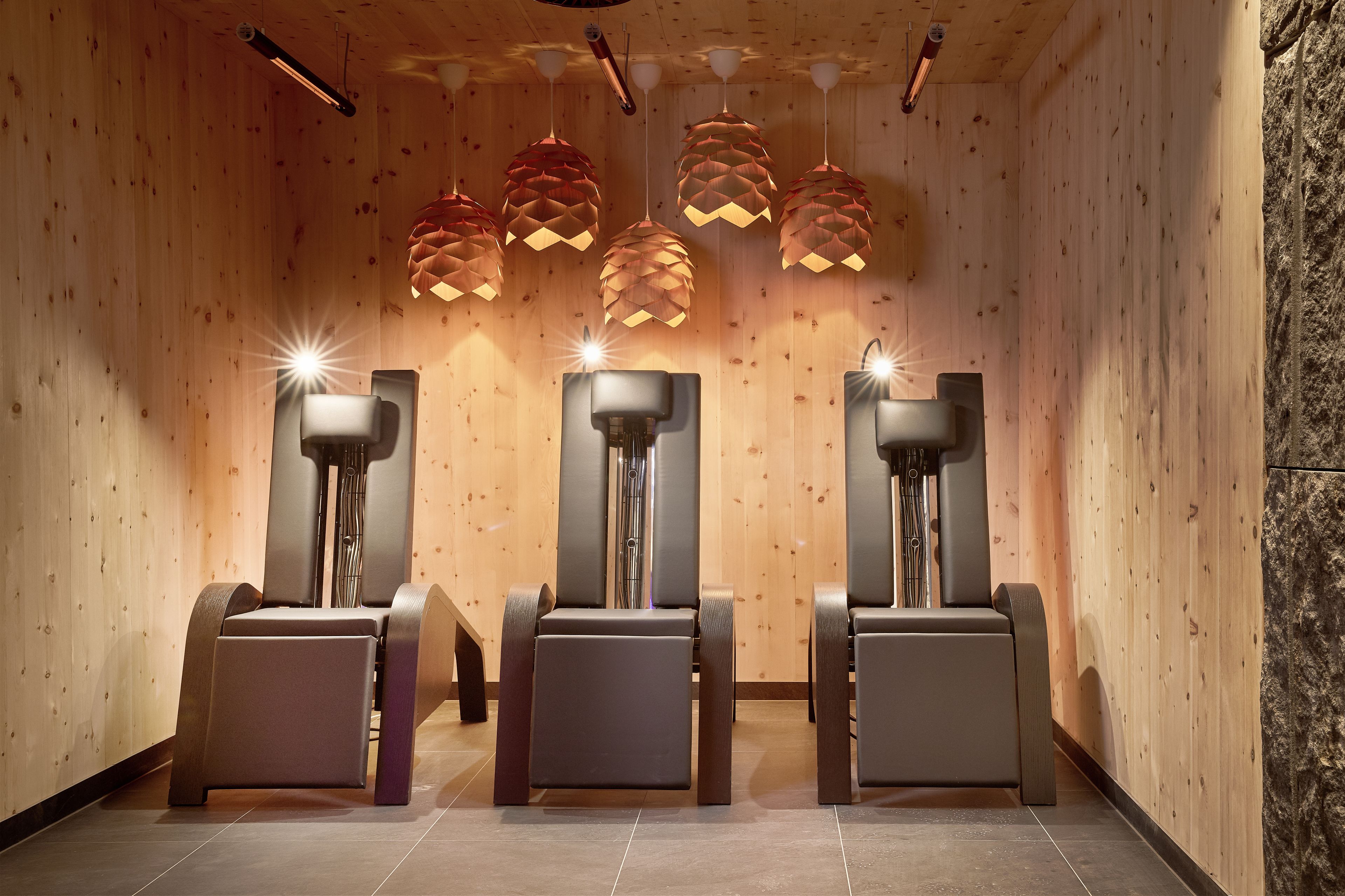 A spa room with wooden walls, three massage chairs, and pendant lights.