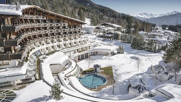 A snow-covered resort with a pool, multiple balconies, and a mountainous backdrop.