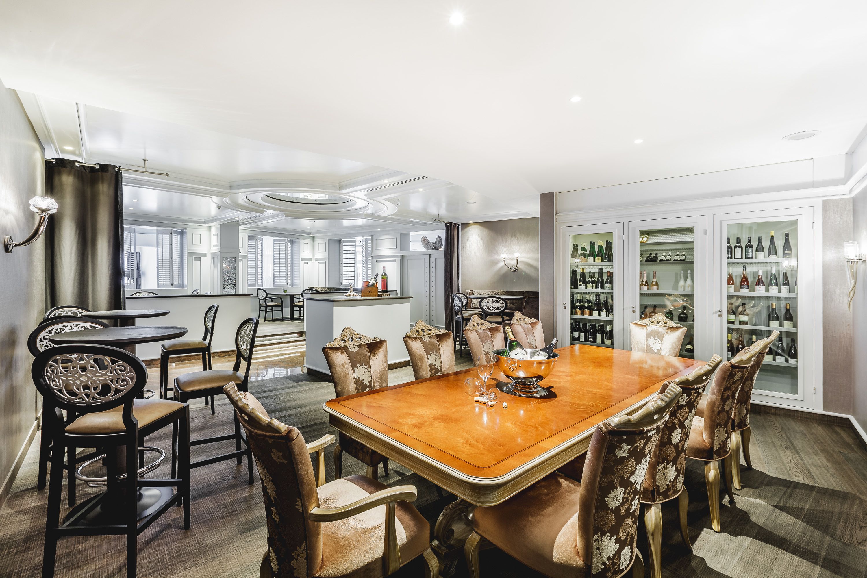 A dining area with a wooden table and upholstered chairs, a bar area with a minibar, and a wine display cabinet.