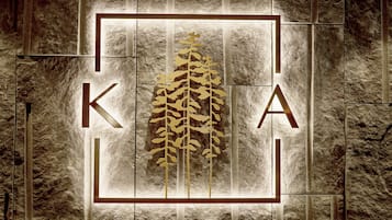 A logo with the letters "K" and "A" and a stylized plant in the center, set against a textured stone wall.