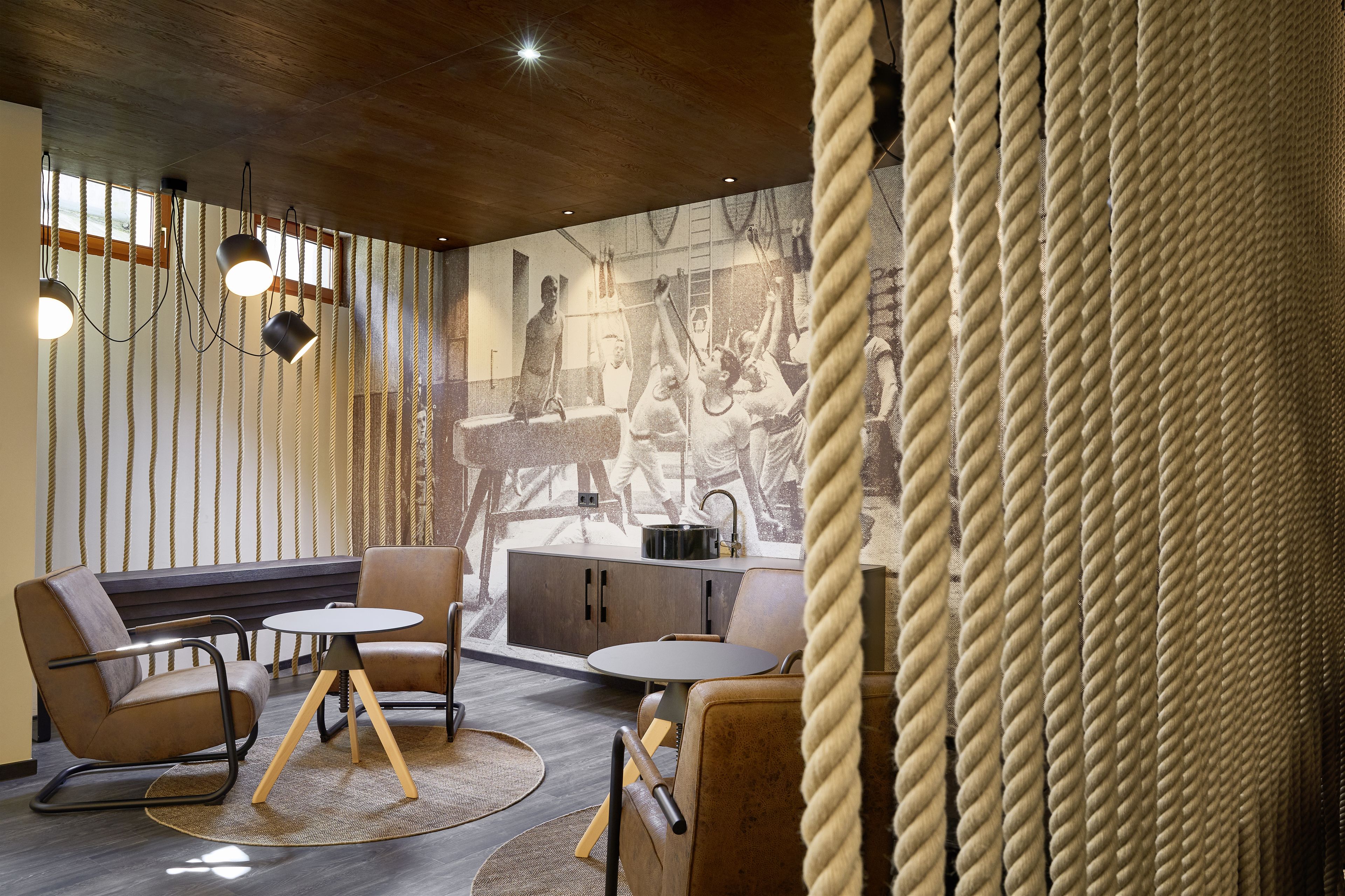 Un interno moderno con un tavolo rotondo e poltrone in pelle, un soffitto in legno e un pannello decorativo con corde.