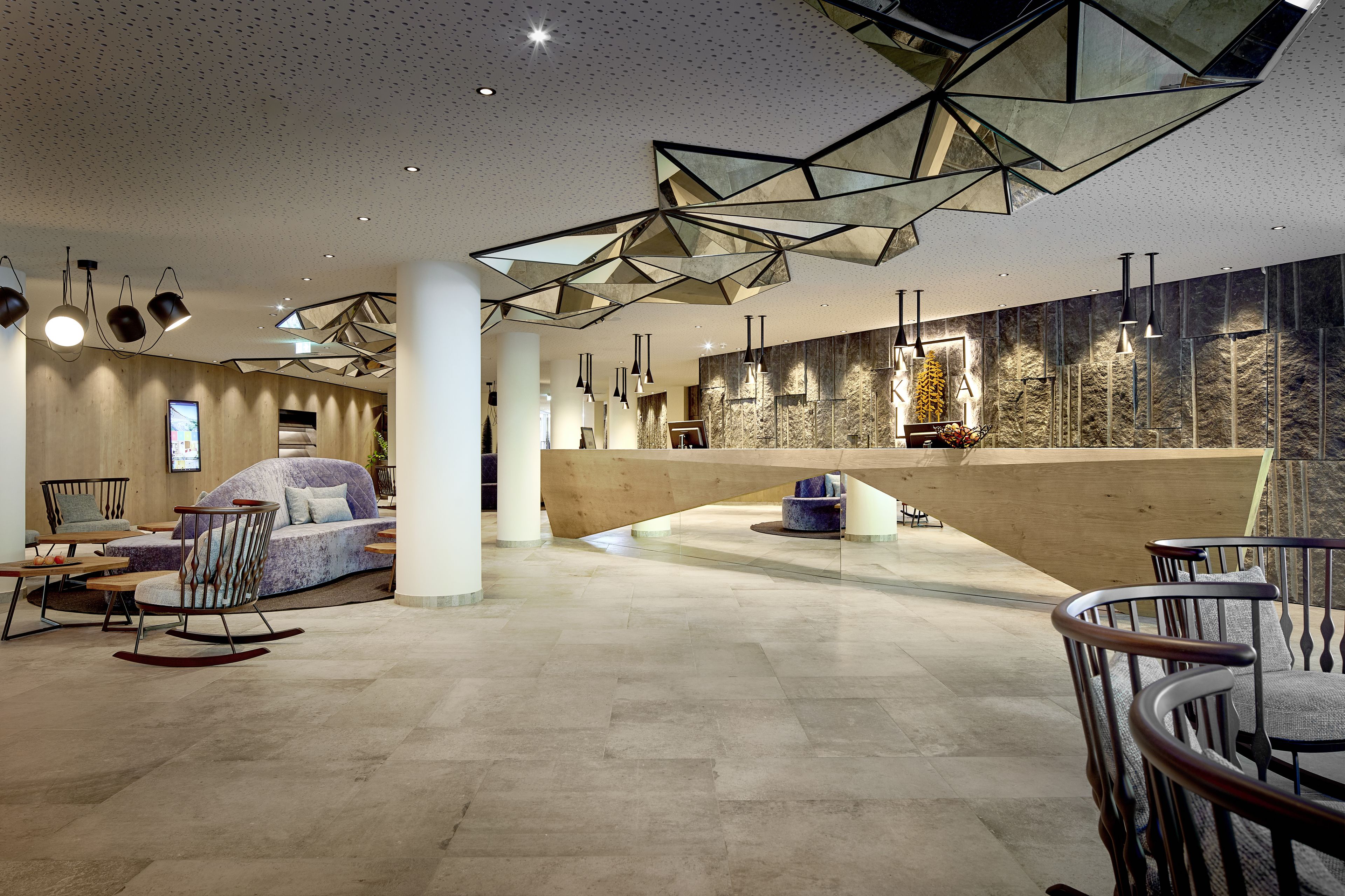 A spacious lobby with a modern design, featuring a large wooden bench, a sofa, and a dining area with chairs.
