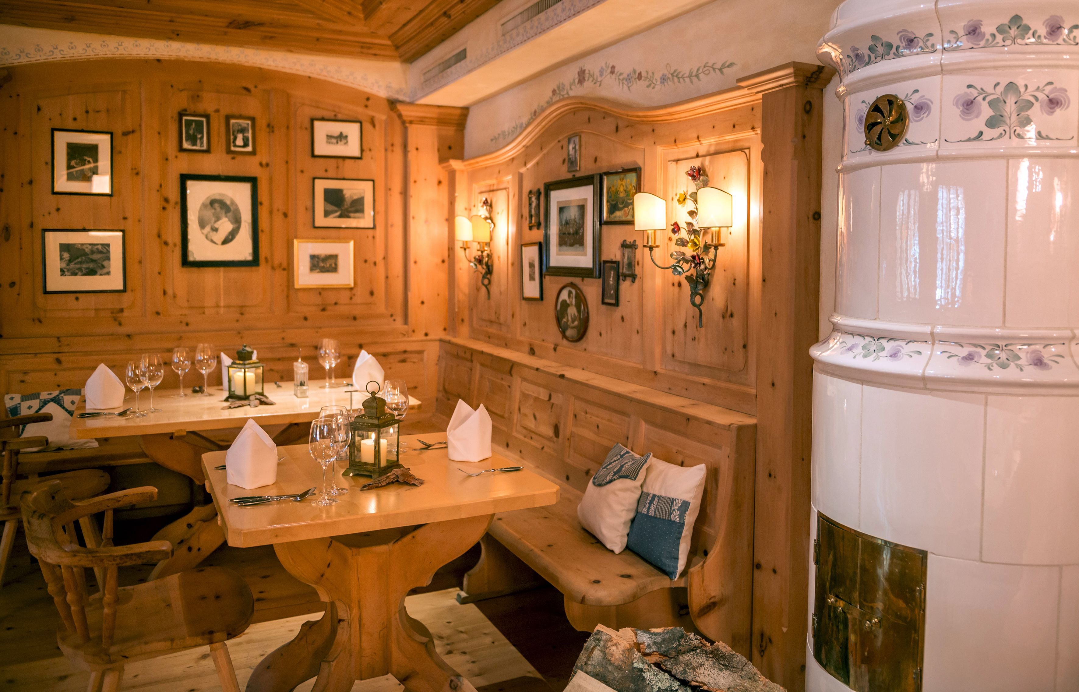 A wooden dining area with a wooden table set for two, benches, and wall-mounted picture frames.