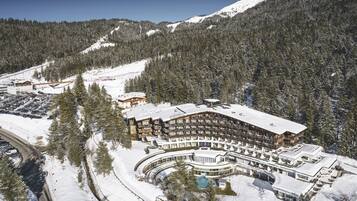 Ein großes, mehrstöckiges Hotel mit geschwungener Fassade, umgeben von schneebedeckten Bergen und Bäumen.
