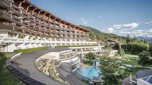 Un hotel con varios balcones, piscina y montañas al fondo.