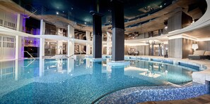 Une vaste piscine intérieure à l’eau cristalline, entourée d’une architecture moderne et de plusieurs niveaux de balcons.