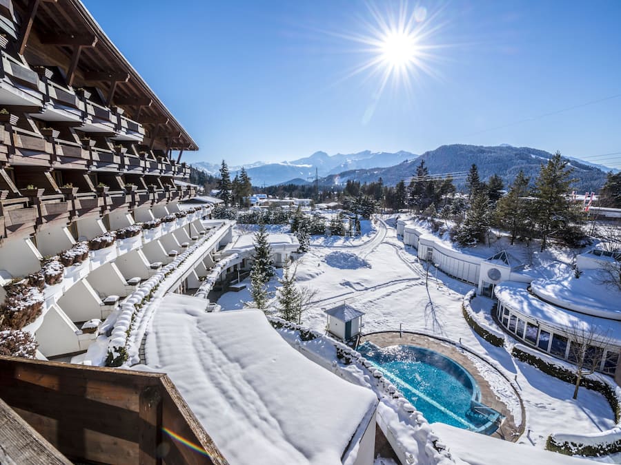 A resort with a pool surrounded by snow-covered grounds, a mountain backdrop, and a clear sky.