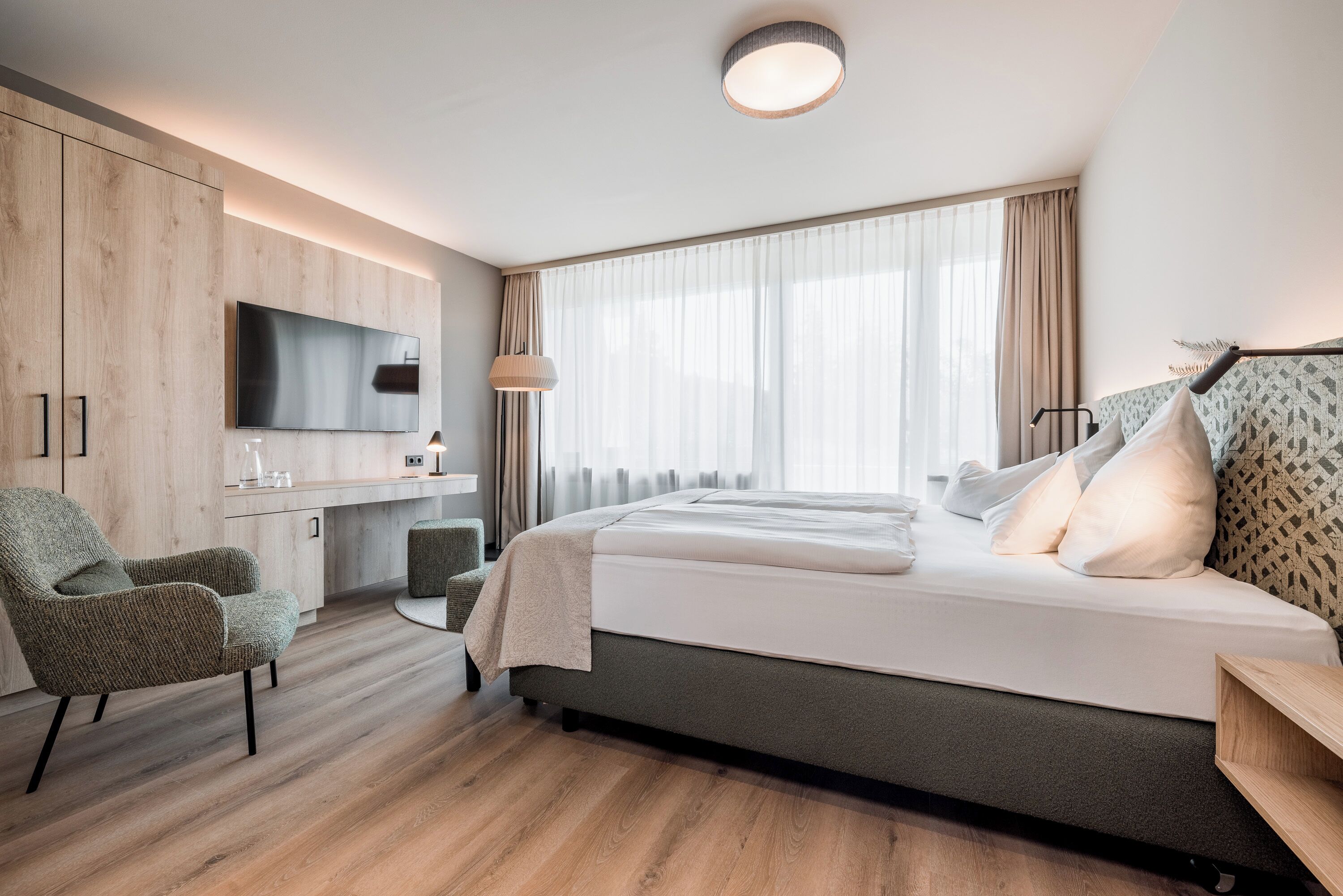 Une chambre d’hôtel moderne équipée d’un lit, d’un bureau, d’une chaise, d’une télévision et d’une grande fenêtre avec des rideaux.